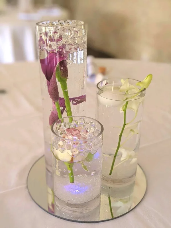Wedding table centrepiece, comprising cylindrical vases arranged with purple calla lilies, white orchid and a pink flower.