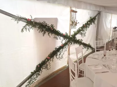 Végétalisation murale en forme de croix avec du ruscus, du lierre et de petites roses roses pour une décoration de salle.